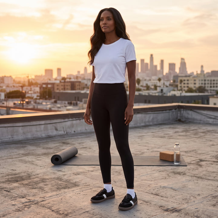 Schwarze Sneaker am Model, schwarze Leggings, weißes T-Shirt, Rooftop-Stadtpanorama