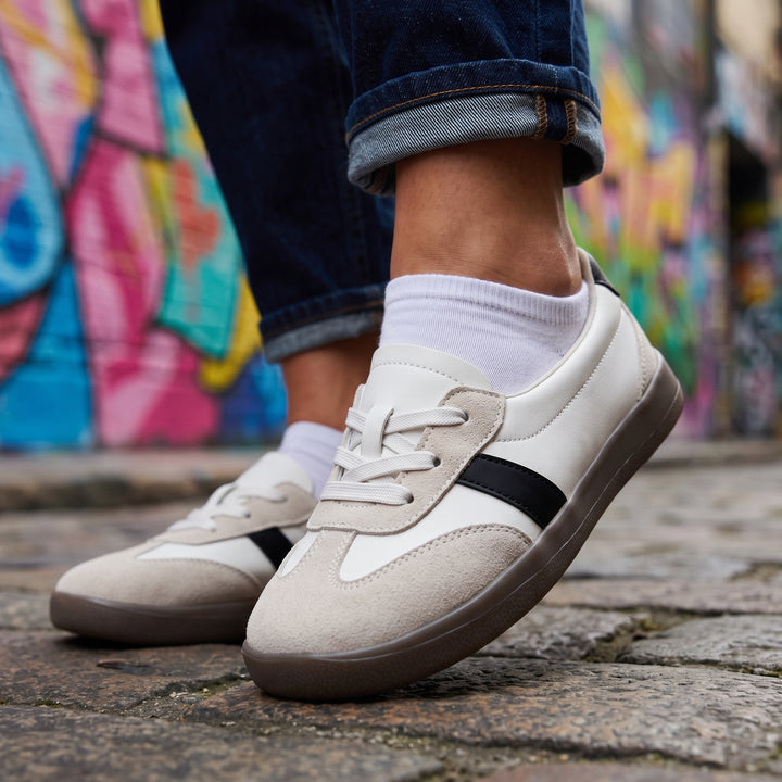 Weiß-Beige Sneaker am Fuß getragen, Jeans aufgekrempelt, Graffiti-Straße, Nahaufnahme