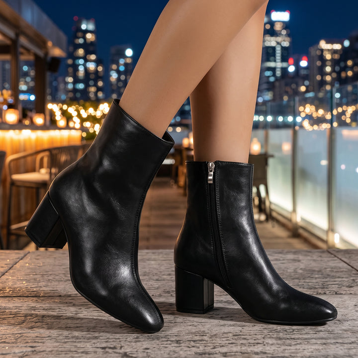 Schwarze Stiefelette mit Glattleder-Optik am Fuß – Seitenansicht mit Stadtkulisse
