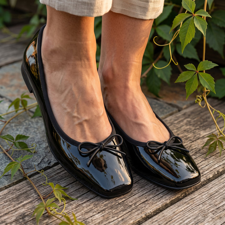 Schwarze Lackleder-Ballerinas an Füßen, Outdoor-Setting mit Rankenpflanzen