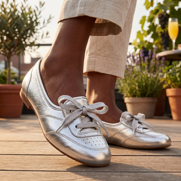 Silberne Damen-Ballerina am Fuß auf Holzterrasse, kombiniert mit beiger Leinenhose