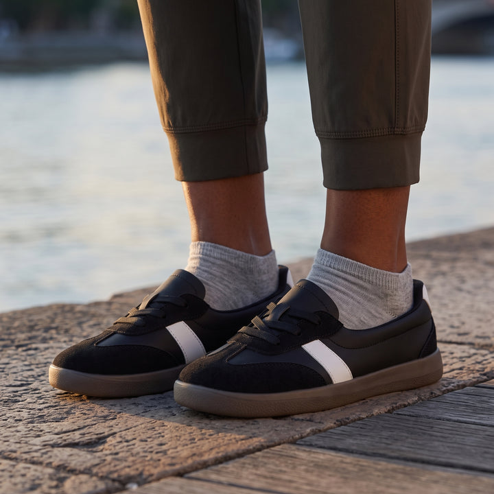 Schwarze Sneaker am Fuß, Olivgrün-Hose, graue Socken, Flussufer bei Sonnenuntergang