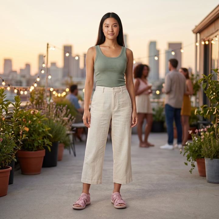 Frau in Leinenhose trägt rosa orthopädische Sandalen auf Dachterrasse bei Sonnenuntergang