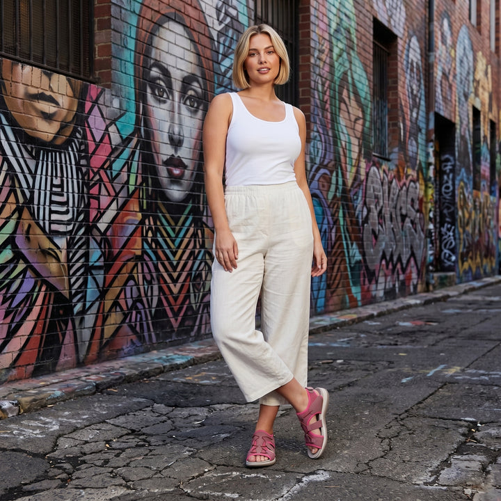 Frau trägt orthopädische Sandalen in Pink zu weißem Top und beiger Culotte, Straßenkulisse