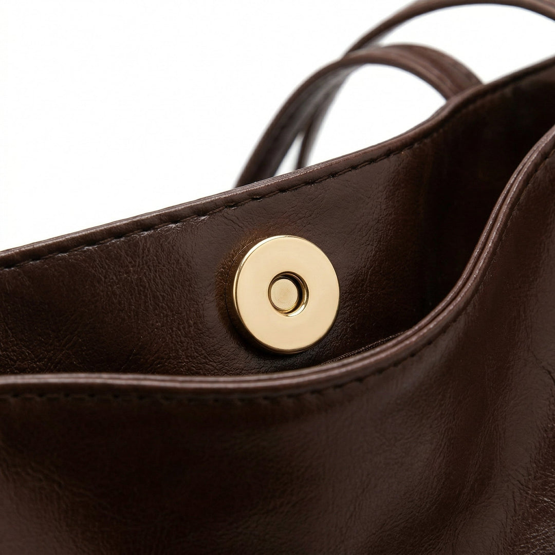 Nahaufnahme goldener Magnetknopf-Verschluss an dunkelbrauner Tasche